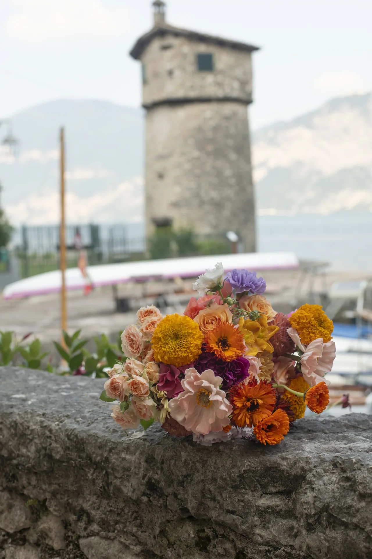 A vibrant summer bouquet resting on a stone wall by Lake Garda