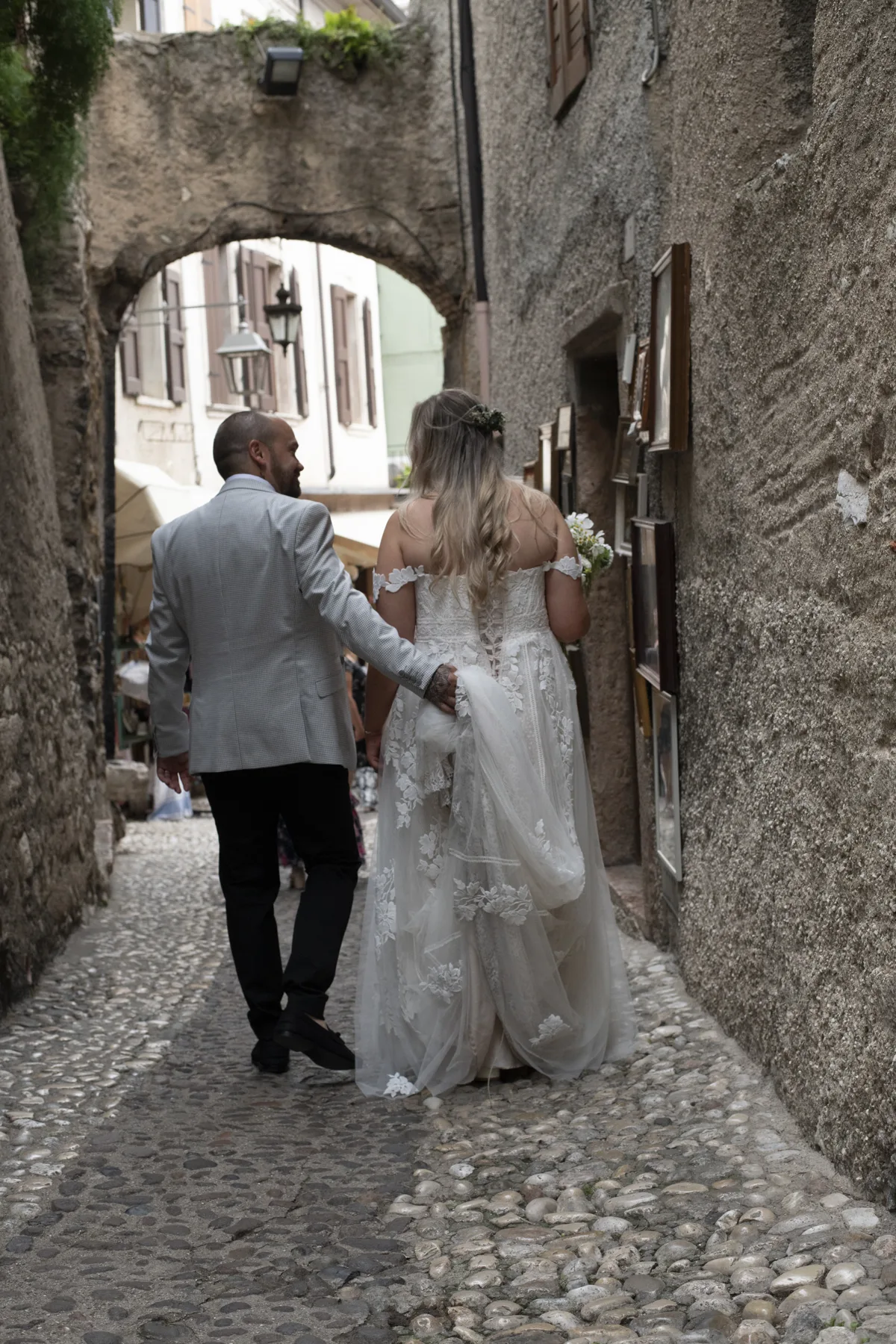 A couple walking hand in hand beneath a stone archway