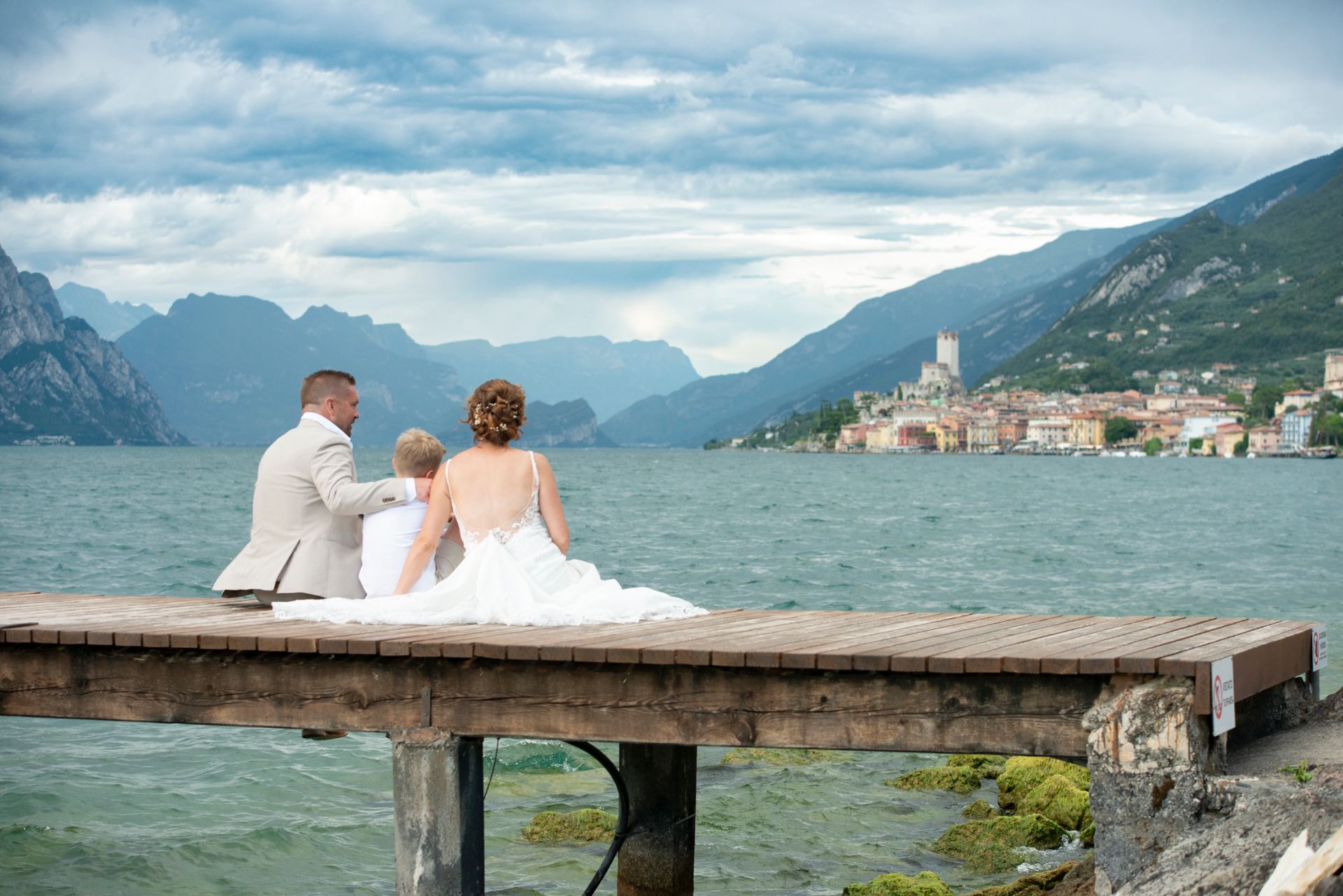 A couple standing on a wooden jetty looking out across Lake Garda